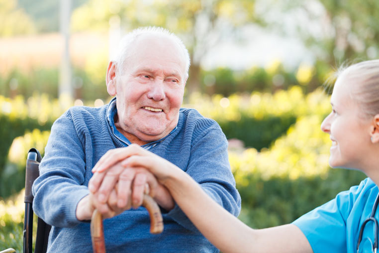 An older man in a wheelchair smiles in conversation with his female carer
