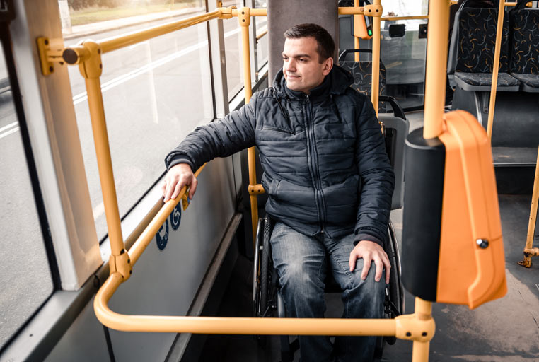 A man sat in a wheelchair looks out the window, whilst travelling on a bus.